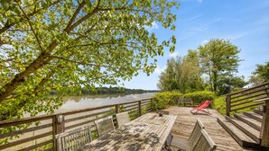 A wooden deck with a table and chairs, overlooking a calm lake and surrounded by greenery.