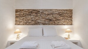 Ein Bett mit weißen Leinen, zwei Nachttischlampen und einem Kopfteil aus Stein.