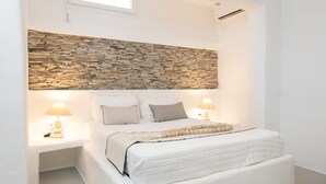Ein Schlafzimmer mit einem Bett, das ein Kopfstück aus Stein hat, weißer Bettwäsche, zwei Nachttischlampen und einer Hängeleuchte.