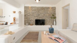 Ein modernes Wohnzimmer mit Steinwand, einem Flachbildfernseher, einem Holztisch mit Zeitschriften, einem weißen Sofa und einem kleinen Teppich.