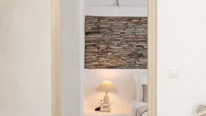 Ein schmaler Flur führt zu einem Schlafzimmer mit Steinsandsteinwand, einer Nachttischlampe und einem Bett.