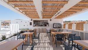 Een terras met houten tafels en stoelen, een bar met flessen op de planken, en uitzicht op het landschap.