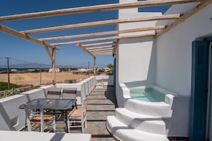 Uma área de estar coberta ao ar livre com piscina, paredes brancas e vista para o mar.