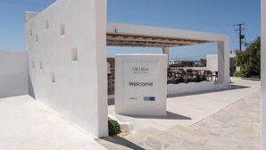 Een wit gebouw met een bord waarop staat 'IRIDA VACATION SUITES Welkom by JNMgroup' en een patio met tafels en stoelen.