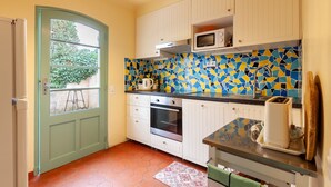 Een keuken met witte kastjes, een magnetron, een oven en een raam met uitzicht op groen.