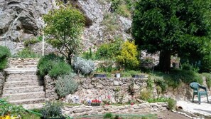 A garden with stone steps leading up to a rocky area, surrounded by various plants and trees.