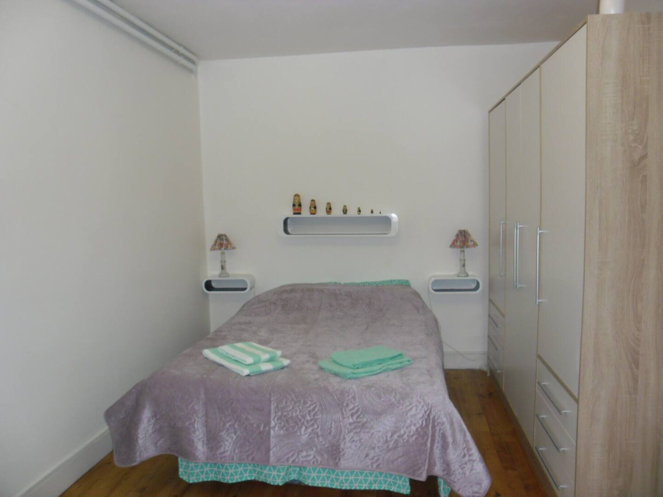 Un dormitorio con cama, dos mesitas de noche, un armario y una estantería decorada.