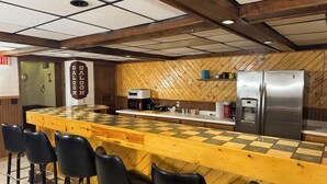 A kitchen with a checkered countertop, a refrigerator, a microwave, and bar stools. - Fenway House Hotel (Fennimore)