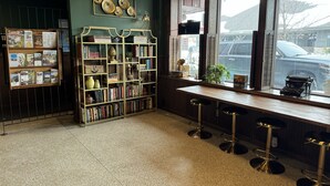 A bar area with a bookshelf, stools, and a window with a view of the street. - Fenway House Hotel (Fennimore)