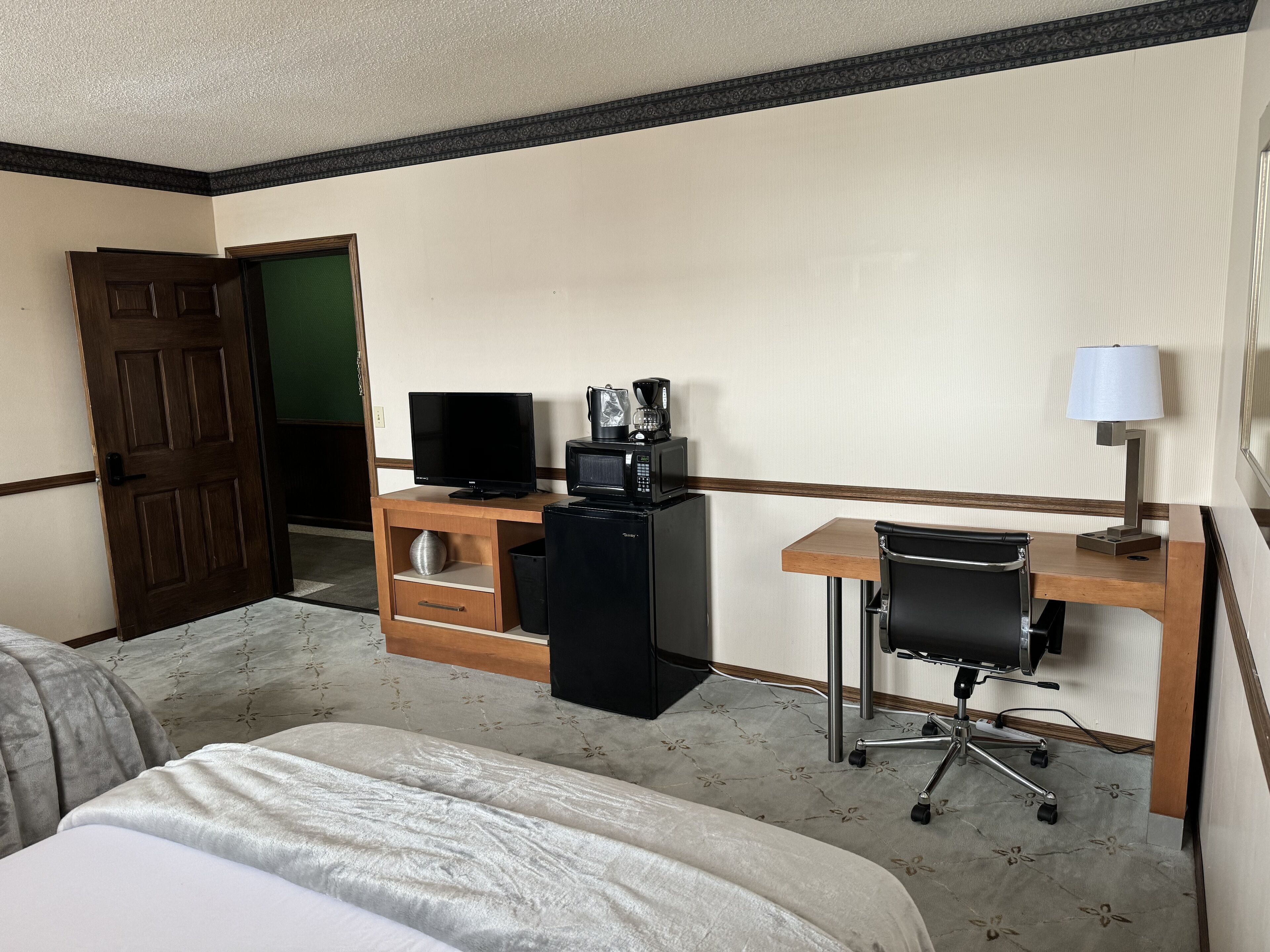 A hotel room with a bed, a desk with a computer, a coffee maker, and a lamp.