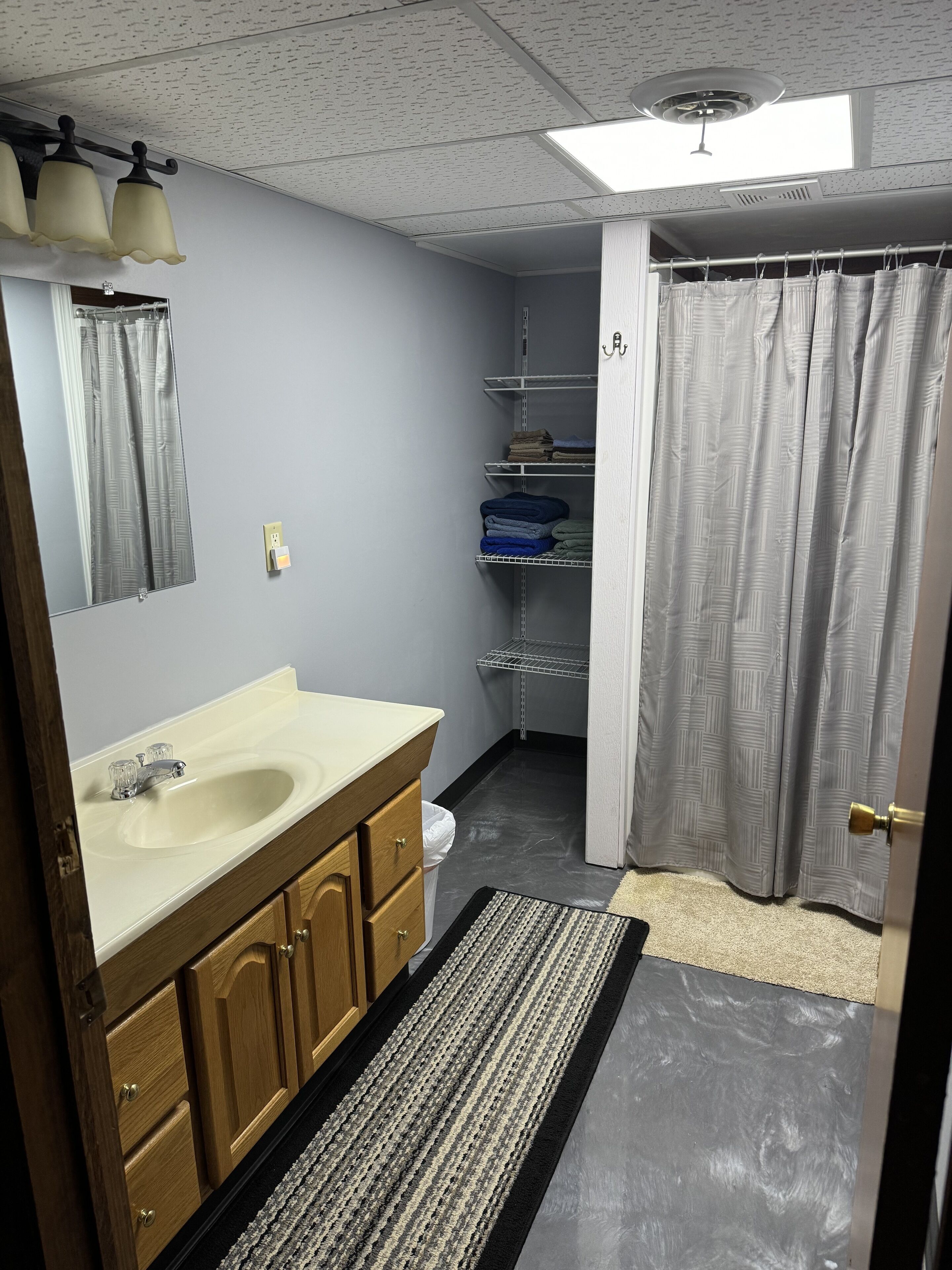 A bathroom with a sink, mirror, shower curtain, and shelves.