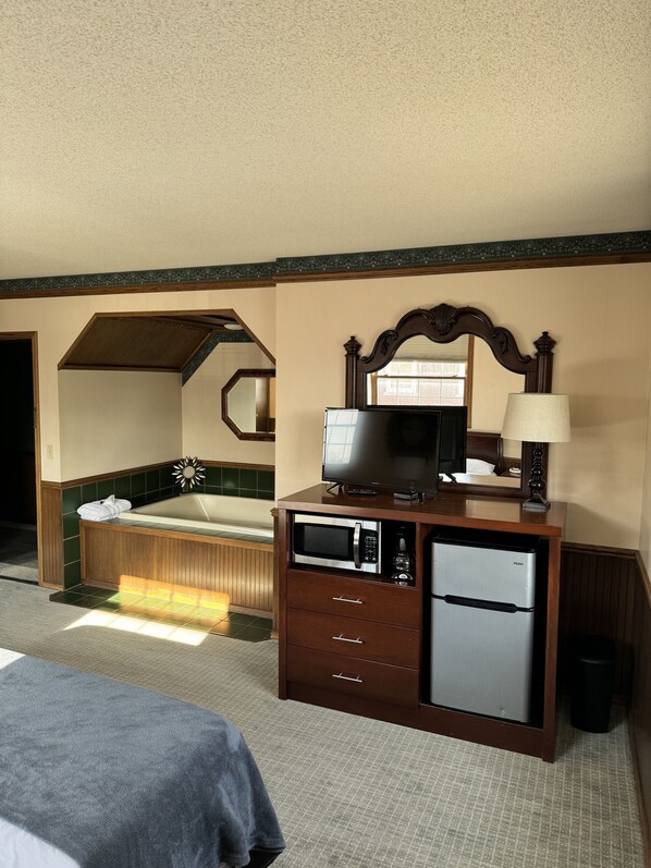 A hotel room with a wooden dresser, a television, a microwave, and a refrigerator.
