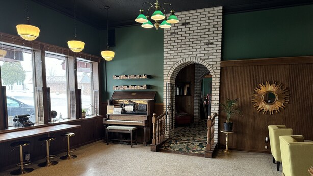A cozy room with a piano, green walls, and a brick fireplace. - Fenway House Hotel (Fennimore)