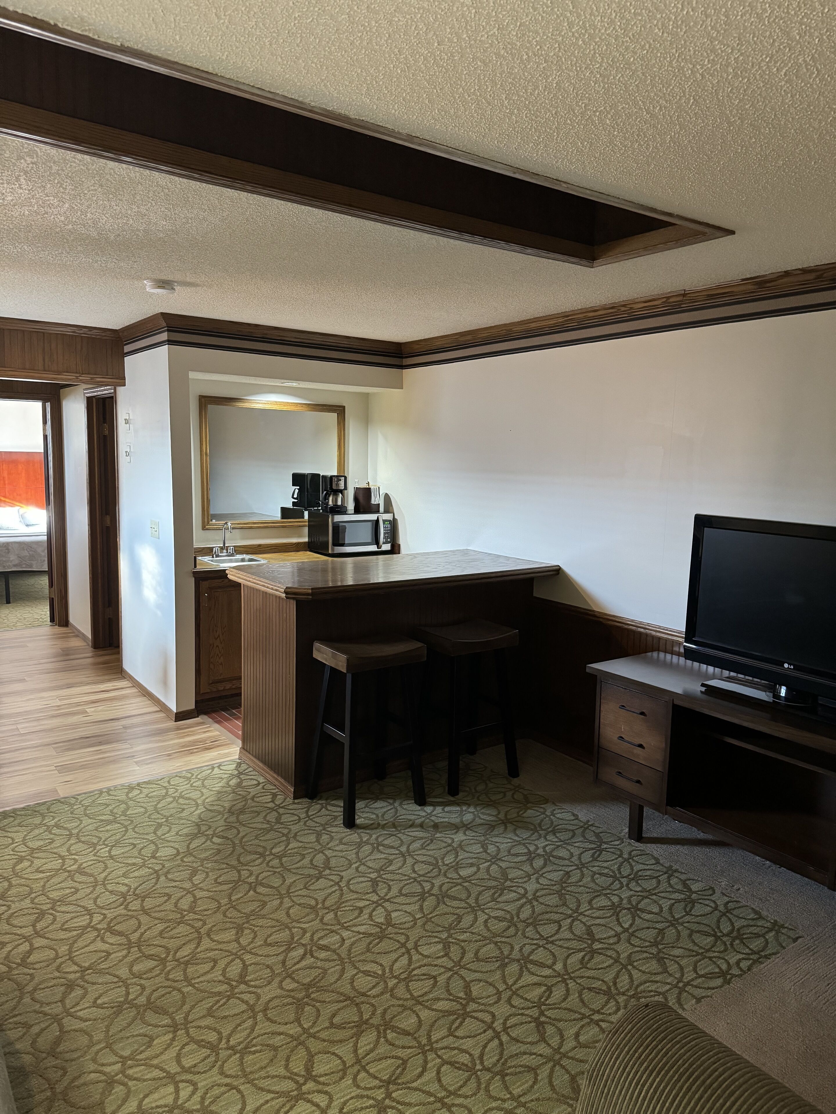 Habitación de hotel con kitchenette, un espejo grande, un televisor de pantalla plana y una alfombra estampada.