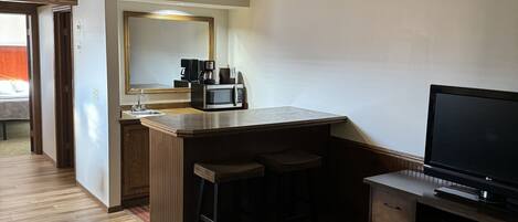 Habitación de hotel con kitchenette, un espejo grande, un televisor de pantalla plana y una alfombra estampada.