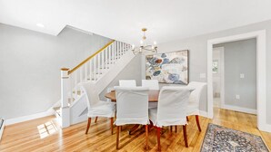 A dining area with a round table, white chairs, a chandelier, and a staircase.