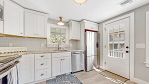 A kitchen with white cabinets, a stainless steel refrigerator, a window, and a door with a glass panel.