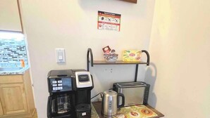A compact kitchenette with a coffee maker, toaster, kettle, and a small shelf with a box of Lipton tea.