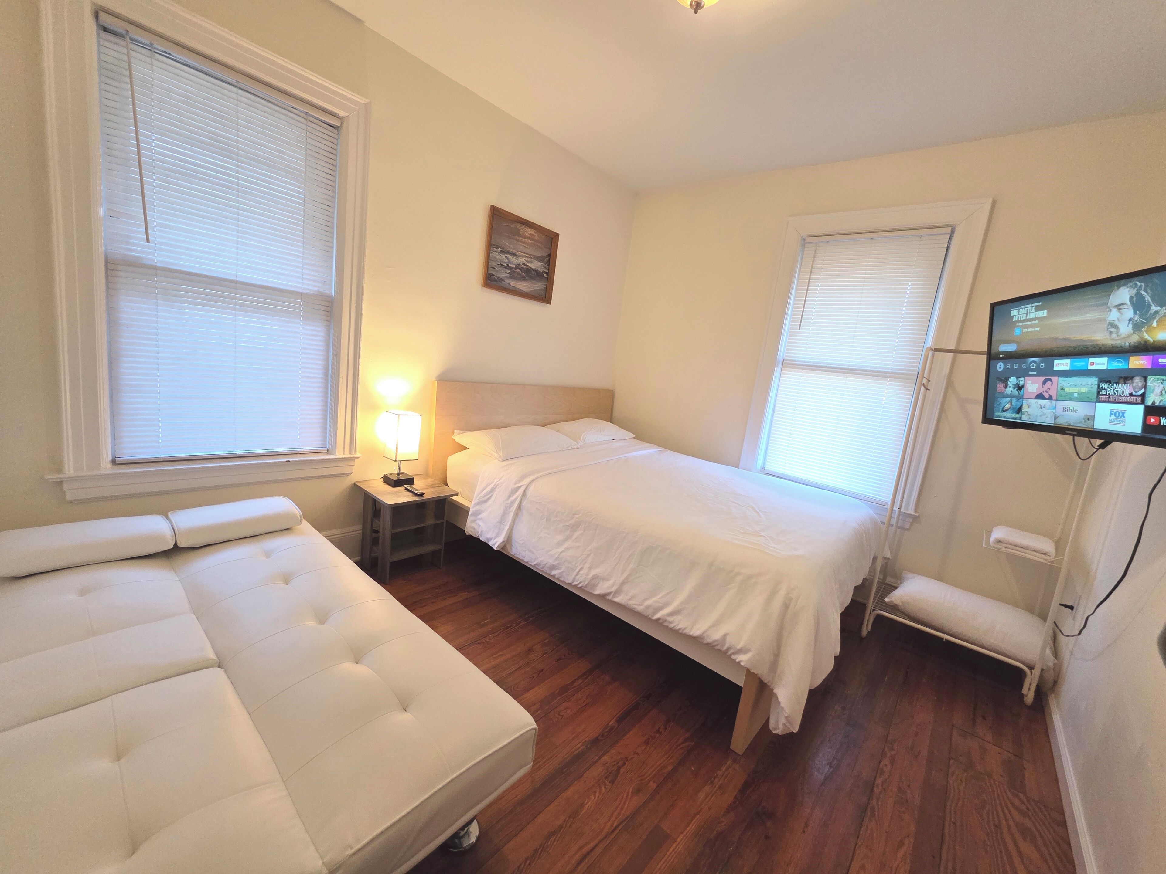 Een slaapkamer met een bed, nachtkastje, lamp, televisie en een bankje.