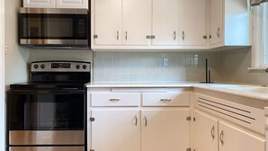 Una cucina con mobili bianchi, un forno in acciaio inox e un forno a microonde.