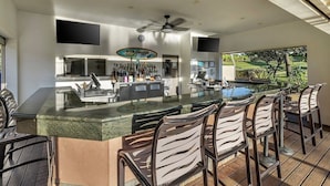 Une cuisine moderne avec un coin bar, un espace salon extérieur et une vue sur la piscine.