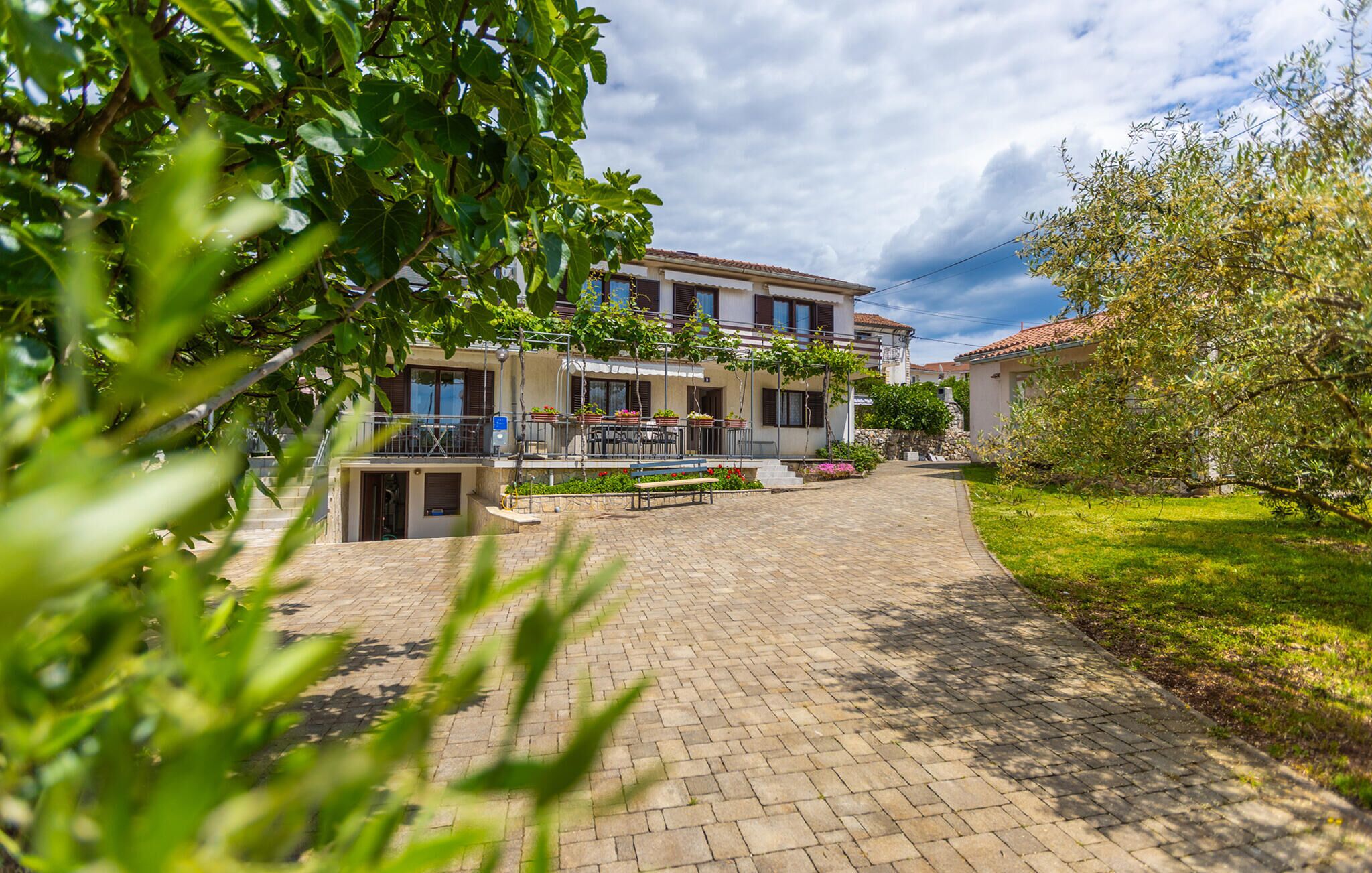 A courtyard with a paved walkway leading to a building with a balcony and outdoor seating area.