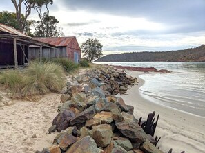 A beach with a wooden structure, a pile of rocks, and a forested hill in the background.