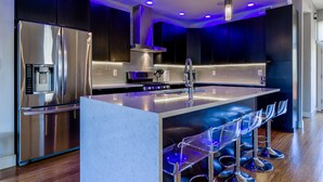 Eine moderne Küche mit Edelstahlkühlschrank, integriertem Backofen und einer Bar mit klaren Hockern.