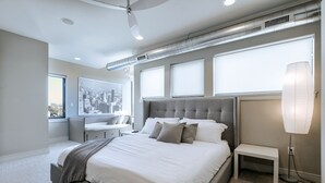 Ein modernes Schlafzimmer mit einem großen Bett, einem Schreibtisch und Blick auf die Stadt.