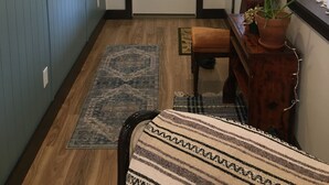 Un pasillo con un banco de madera, una alfombra, una planta en maceta y una estantería con velas y un marco de fotos.