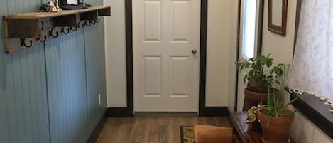 A hallway with a wooden bench, a rug, a potted plant, and a shelf with candles and a picture frame.