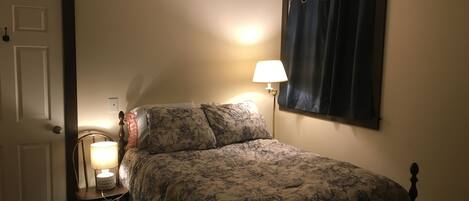 A bedroom with a bed, a nightstand, a lamp, a door, and a window with curtains.