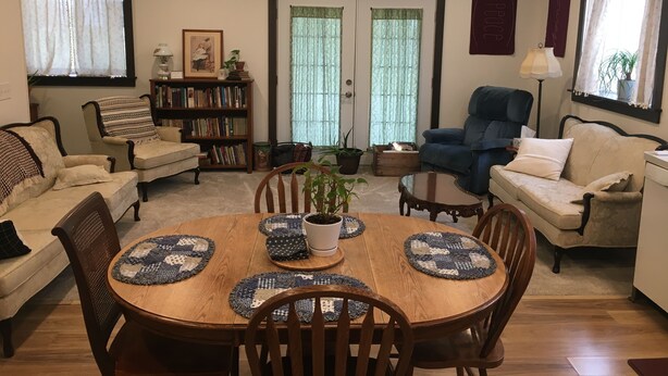 Una sala de estar acogedora con una mesa de comedor, sofás, una estantería y un ventanal con cortinas.