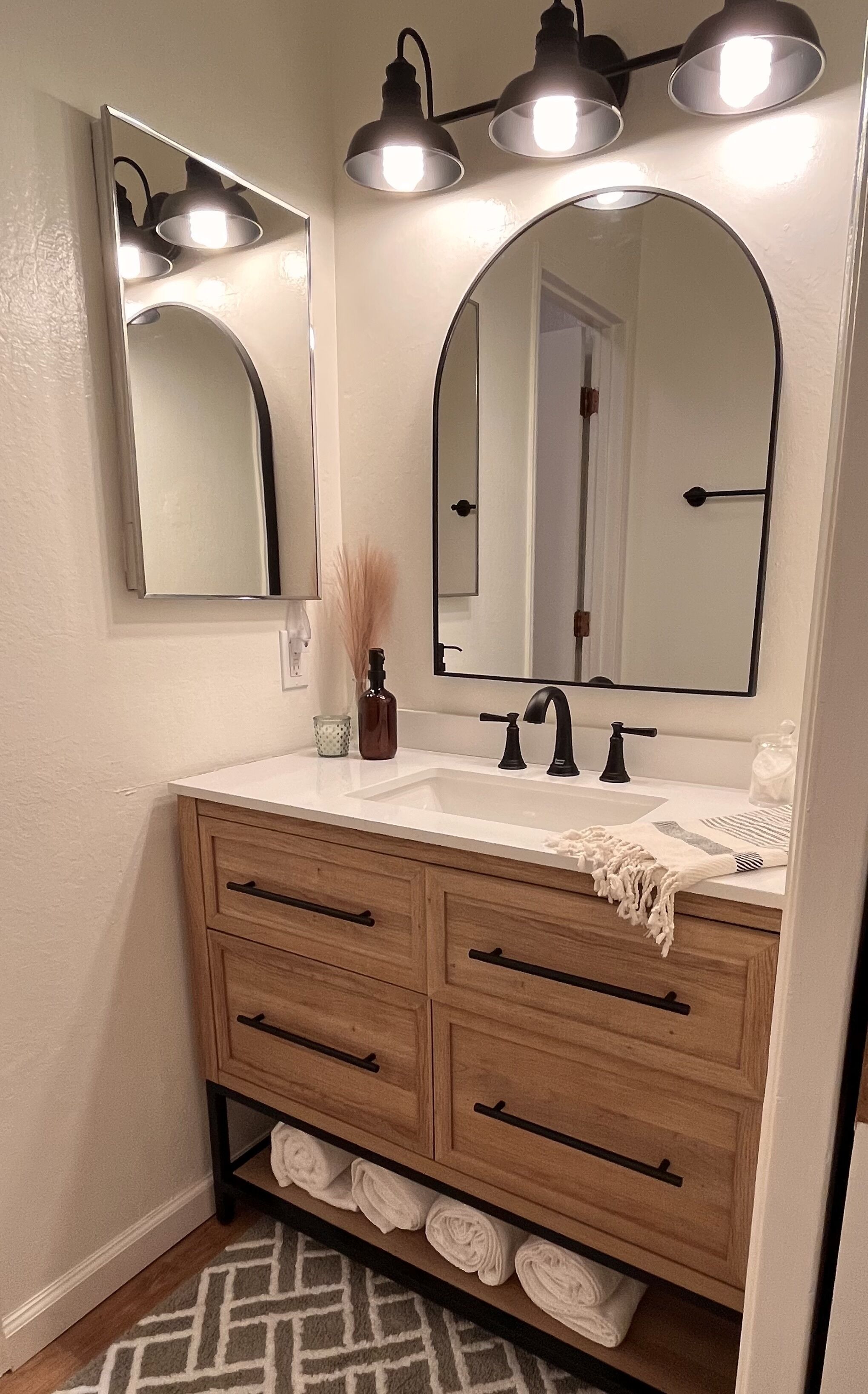 A bathroom with a wooden vanity, a large mirror, and three wall-mounted lights.