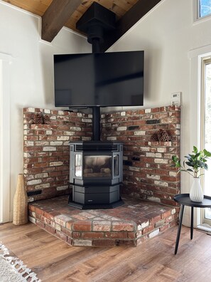 Una habitación de esquina con chimenea de ladrillo, un televisor de pantalla plana montado encima y una mesita con una planta.