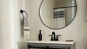Un baño con un lavabo blanco, un espejo redondo y un toallero con una toalla a rayas.