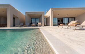 Un área de piscina moderna con agua cristalina, sillas de descanso y un edificio con grandes ventanales.