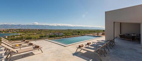 A rooftop pool with lounge chairs, a view of mountains, and a clear sky.