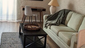 Un soggiorno con divano, tavolino, poltrona, lampada, quadro appeso al muro e condizionatore d'aria.