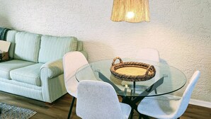 Un soggiorno moderno con un tavolo in vetro, poltrone rivestite in grigio, un cesto intrecciato, un divano a righe e una parete strutturata.