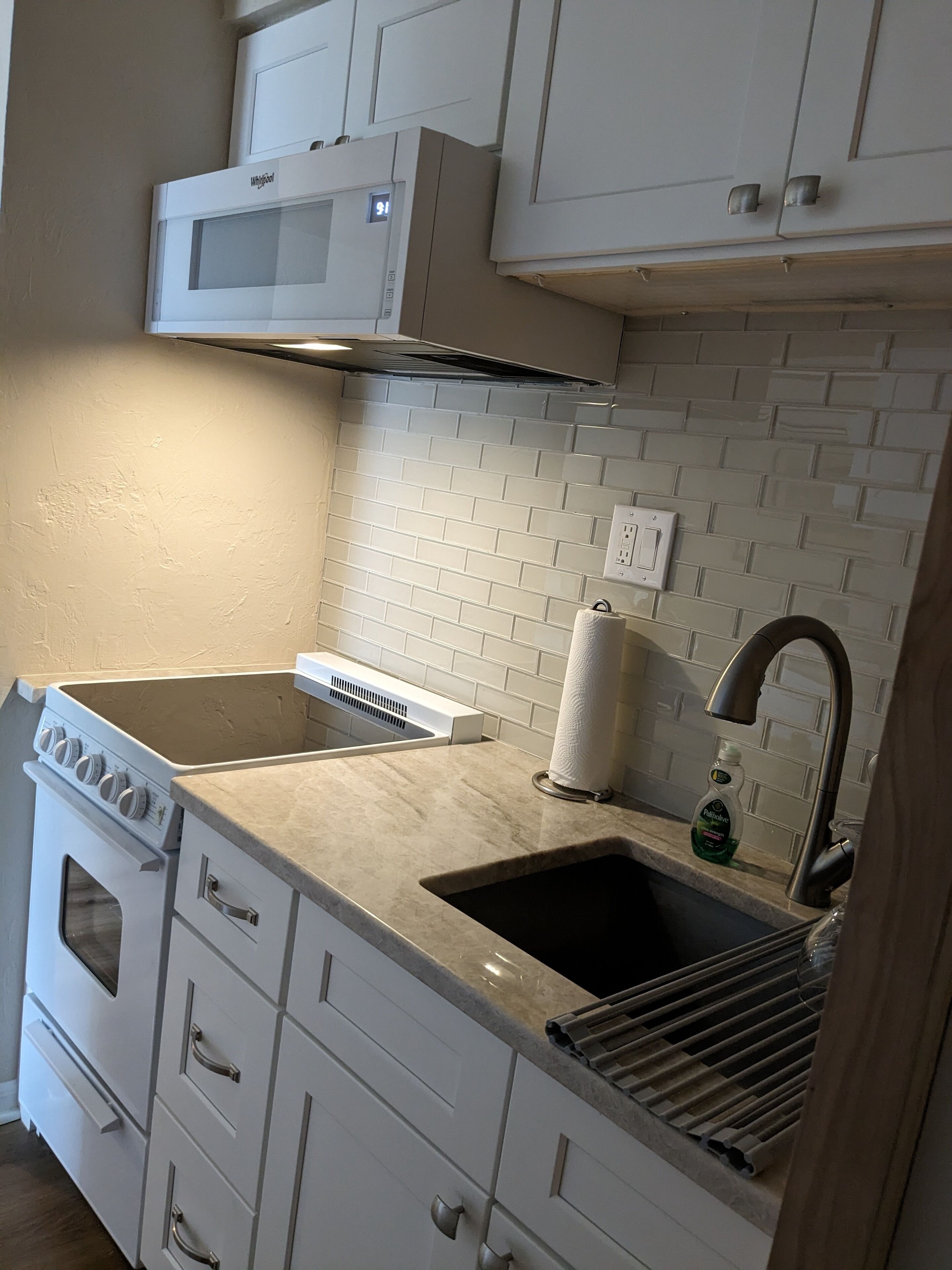 A kitchen with white cabinets, a built-in microwave, a stainless steel range hood, a sink with a faucet, and a dish soap bottle.