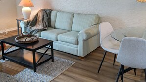 Un soggiorno con divano, tavolino, lampada e un tavolo in vetro con sedie.
