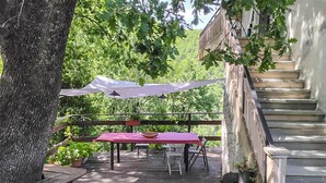 Un'area esterna in legno con tavolo e sedie rossi, immersa nel verde e protetta da una tettoia bianca.