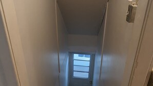 Una escalera estrecha con un pequeño ventanal en la parte superior, que lleva a una puerta.