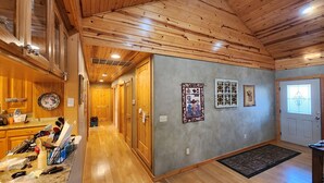 Un interior de madera con una zona de cocina, un pasillo con puertas y una pared decorada con cuadros.