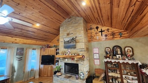 Una sala de estar acogedora con chimenea de piedra, techo de madera y televisor.
