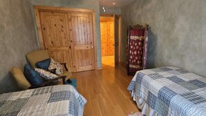 Una habitación con dos camas, una puerta de madera, una silla con cojines y una cortina roja.