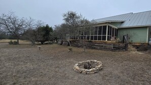 Una cabaña rústica con techo de metal, rodeada por un patio cercado con un brasero de piedra.
