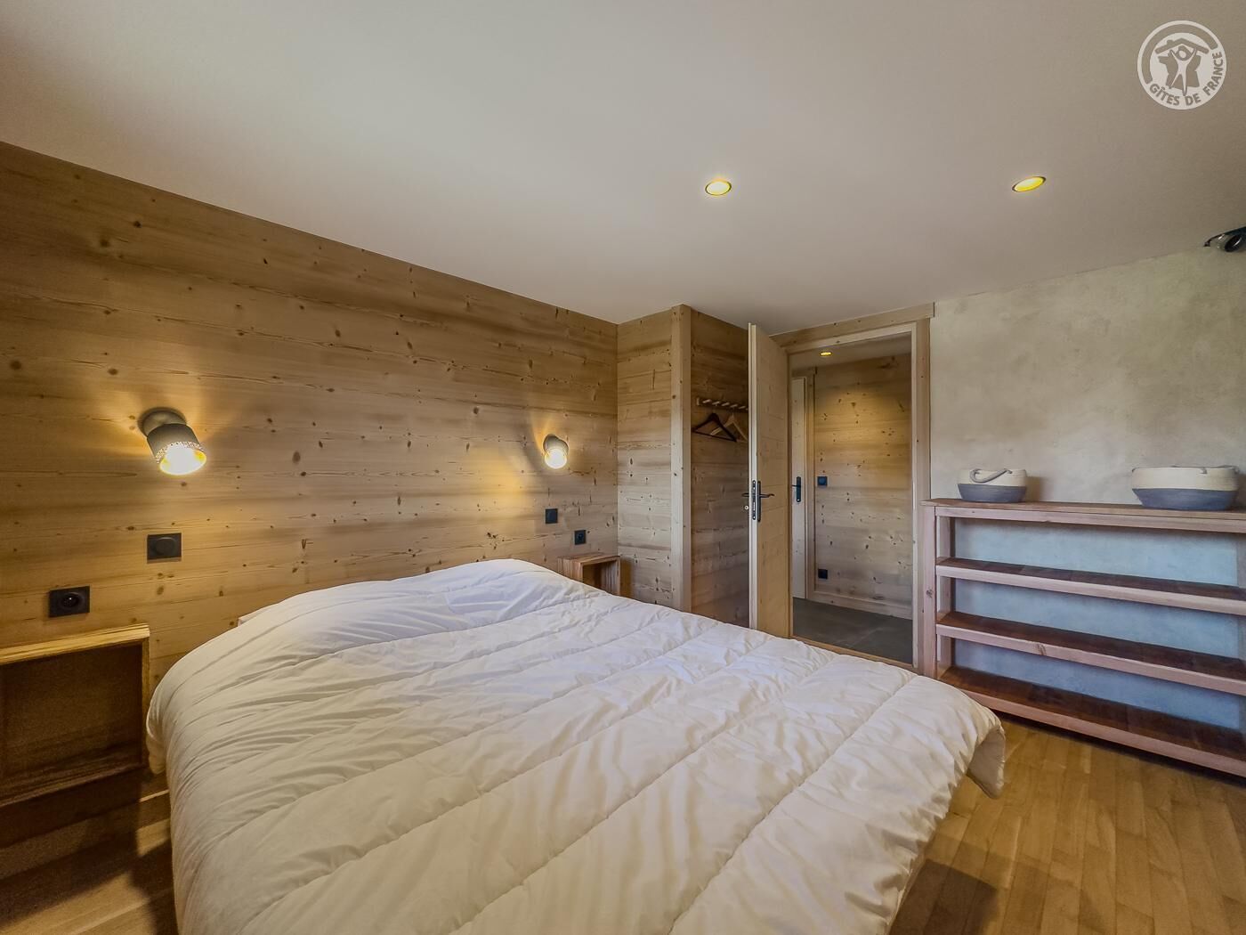 A bedroom with a wooden wall, a bed, bedside tables, and a wardrobe.