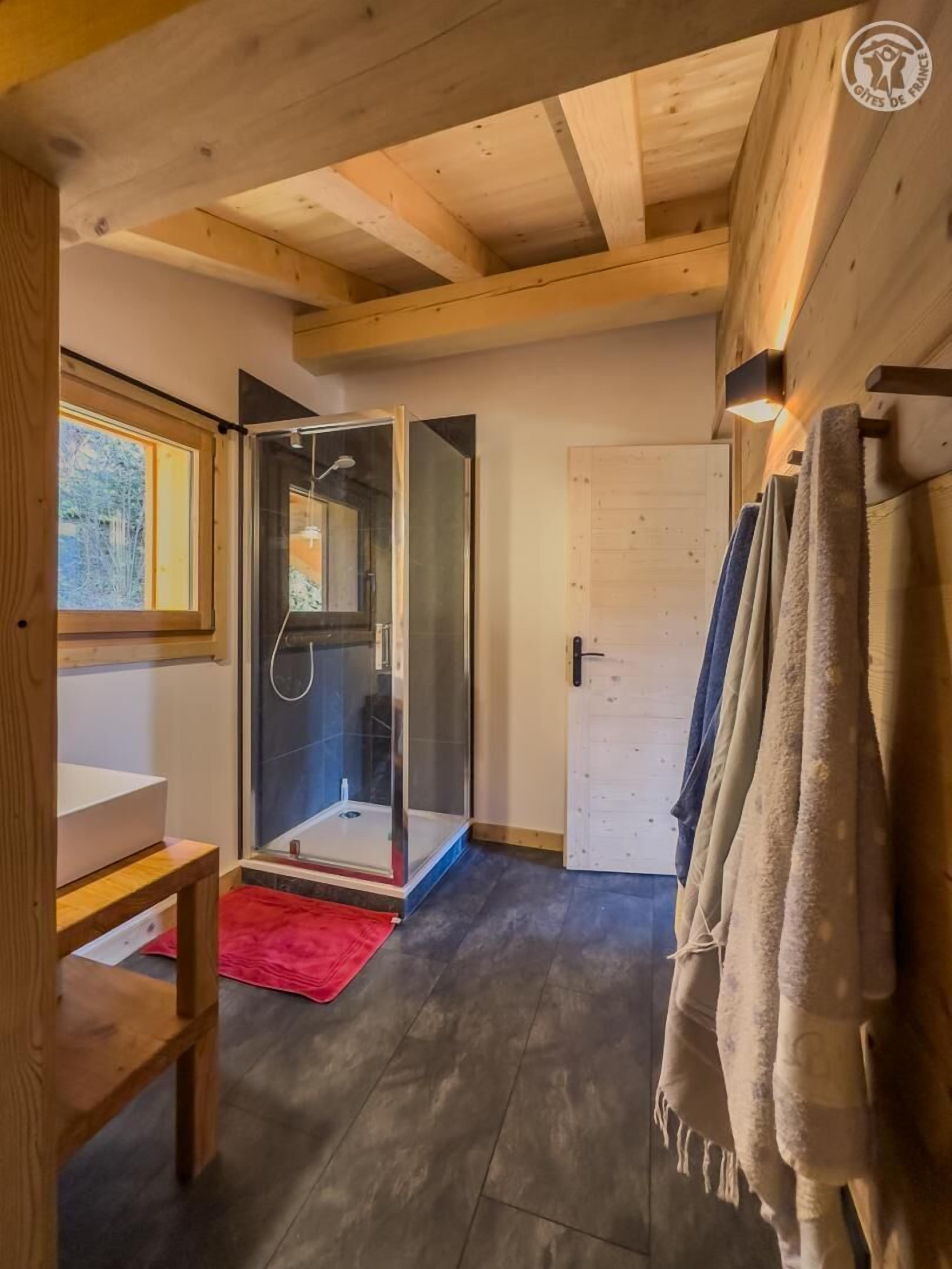 Une salle de bain moderne avec une douche à parois de verre, un banc en bois, un tapis rouge et des serviettes accrochées au mur.